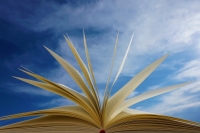 Ein aufgeblaettertes Buch vor einem blauen Himmel