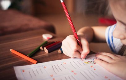Bildausschnitt Kind bei den Hausaufgaben, am Schreiben mit Bunt-, und Bleistiften