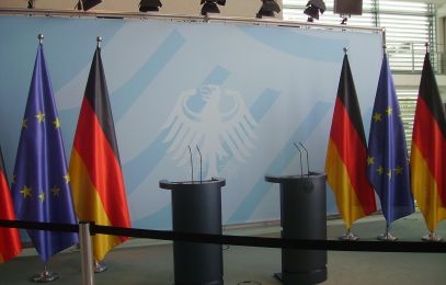 Flaggen der EU und Deutschland neben einem Rednerpult mit Bundesadler im Hintergrund